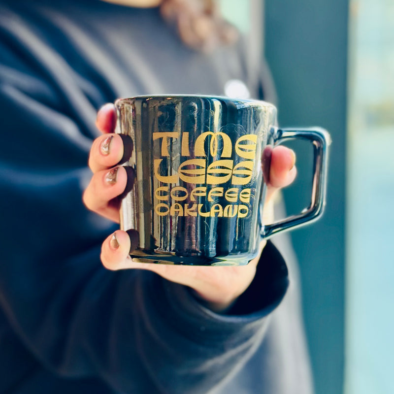 Timeless Coffee Roasters Black Diner Mug with Gold Writing in Person's Hand