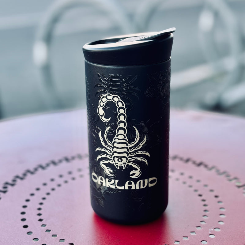 Timeless Coffee Roasters Black Oakland To-Go Tumbler with Gold Scorpion on Red Table