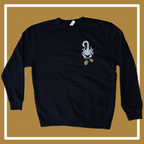 A black crewneck sweatshirt laying on a golden and white background, the front has a white scorpion holding golden acorns in the upper right hand corner (of the photo, left hand corner on the shirt itself); the back reads “Timeless Coffee” in a gold and white font, and “est. 2012, Oakland, CA,” underneath this all is small white acorns. 
